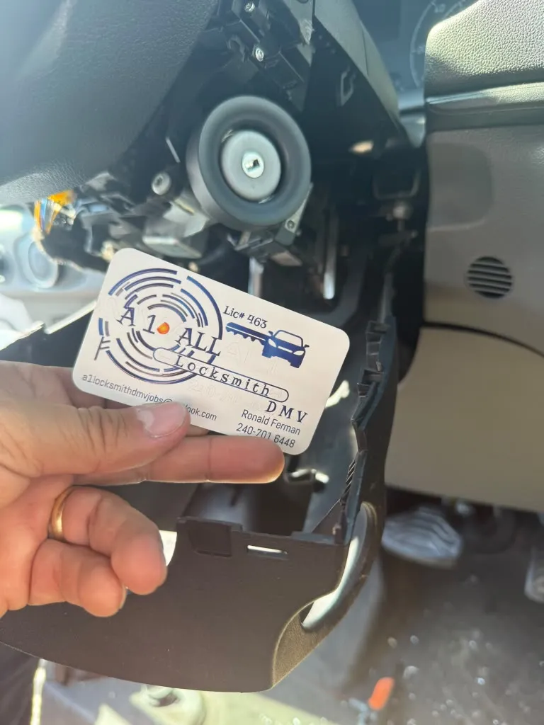 Ignition lock cylinder exposed after removing the steering column cover, beside an A1 All Locksmith DMV business card